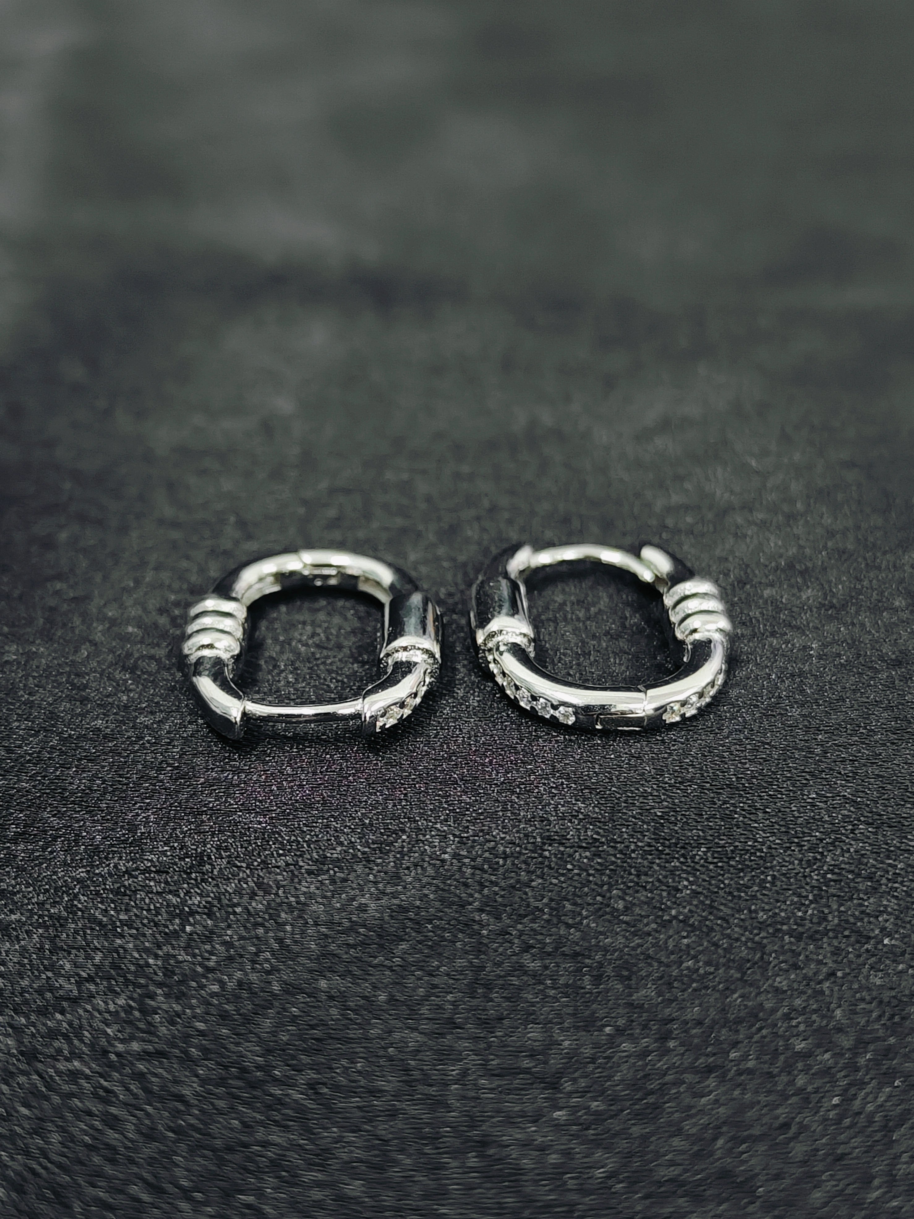 Pair of silver hoop earrings on a black textured surface
